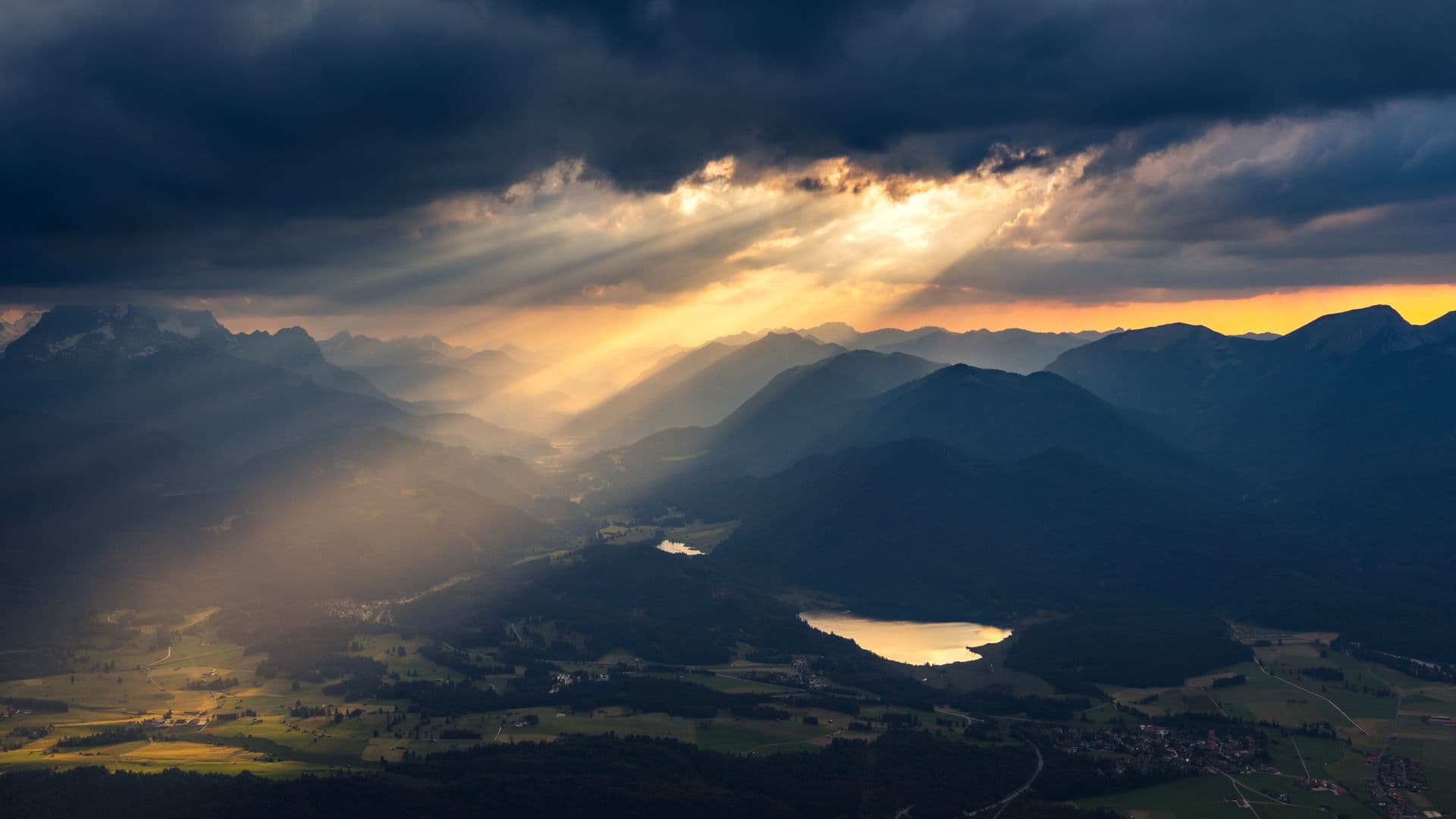 Sunbeams piercing through clouds over a scenic mountain and valley at sunset